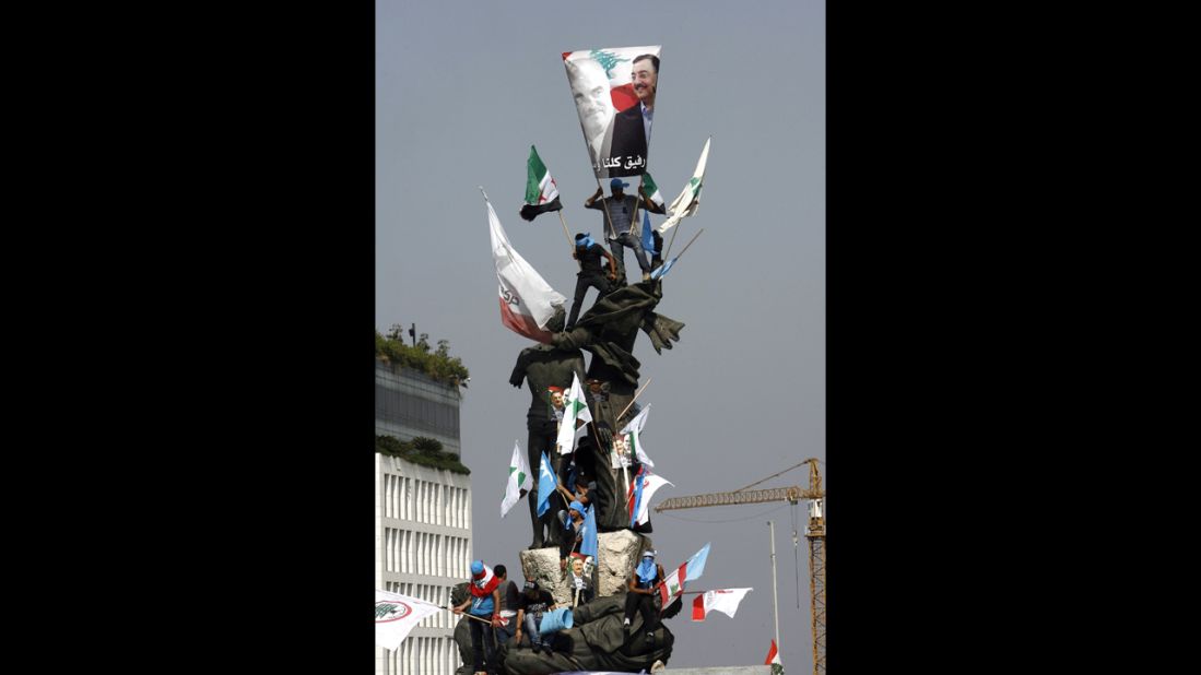 Protesters climb a statue Sunday during the funeral of al-Hassan.