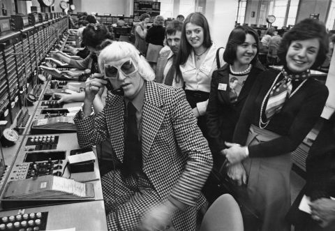 Savile calls from the Wren House International Telephone Exchange in London in 1975 as part of a "Fun And Happiness Weekend," organized by the National Association of Youth Clubs.