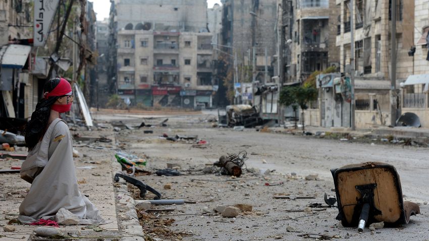 A woman sits on the sidewalk of a debris strewn street in Aleppo, Syria, on October 23.