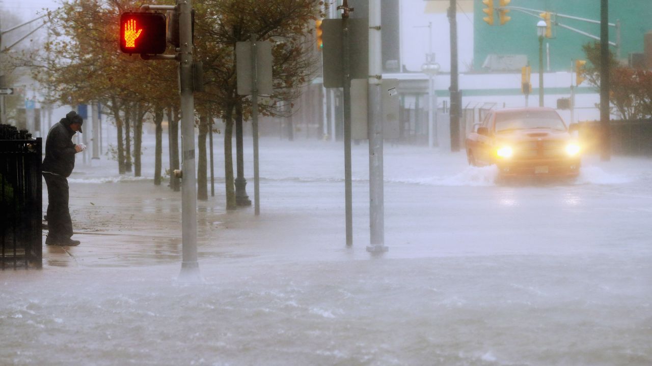 A man stands on the sidewalk Monday as a vehicle drives up a flooded street in Atlantic City.