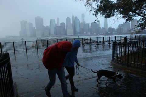 A couple walks in the rain Tuesday, with the East River and the Lower Manhattan skyline as a backdrop.