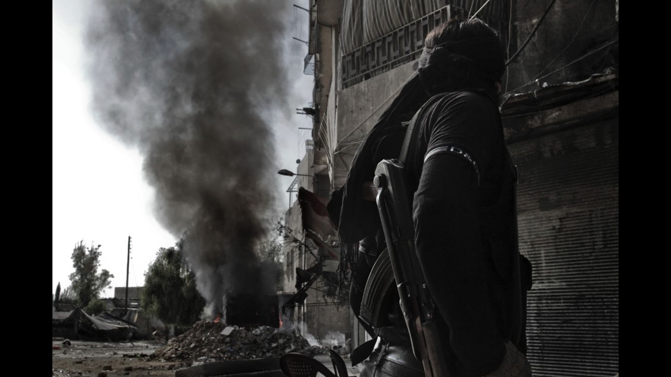 A Syrian rebel fighter looks at smoke billowing from a bus that caught fire after a regime sniper allegedly shot at it in Aleppo on Sunday, October 28.