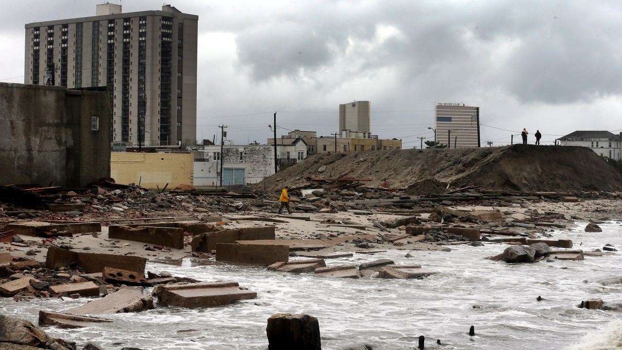 People stand on a mound of construction dirt on Tuesday to view a section of the uptown boardwalk in Atlantic City, New Jersey, that was destroyed by flooding.