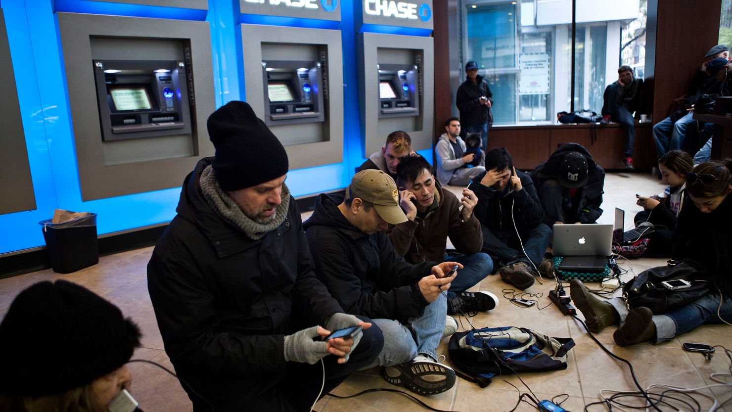 New Yorkers crowd into a Chase Bank ATM kiosk to charge phones and laptops at 40th Street and Third Avenue. 'This is the modern campfire,' one man said.