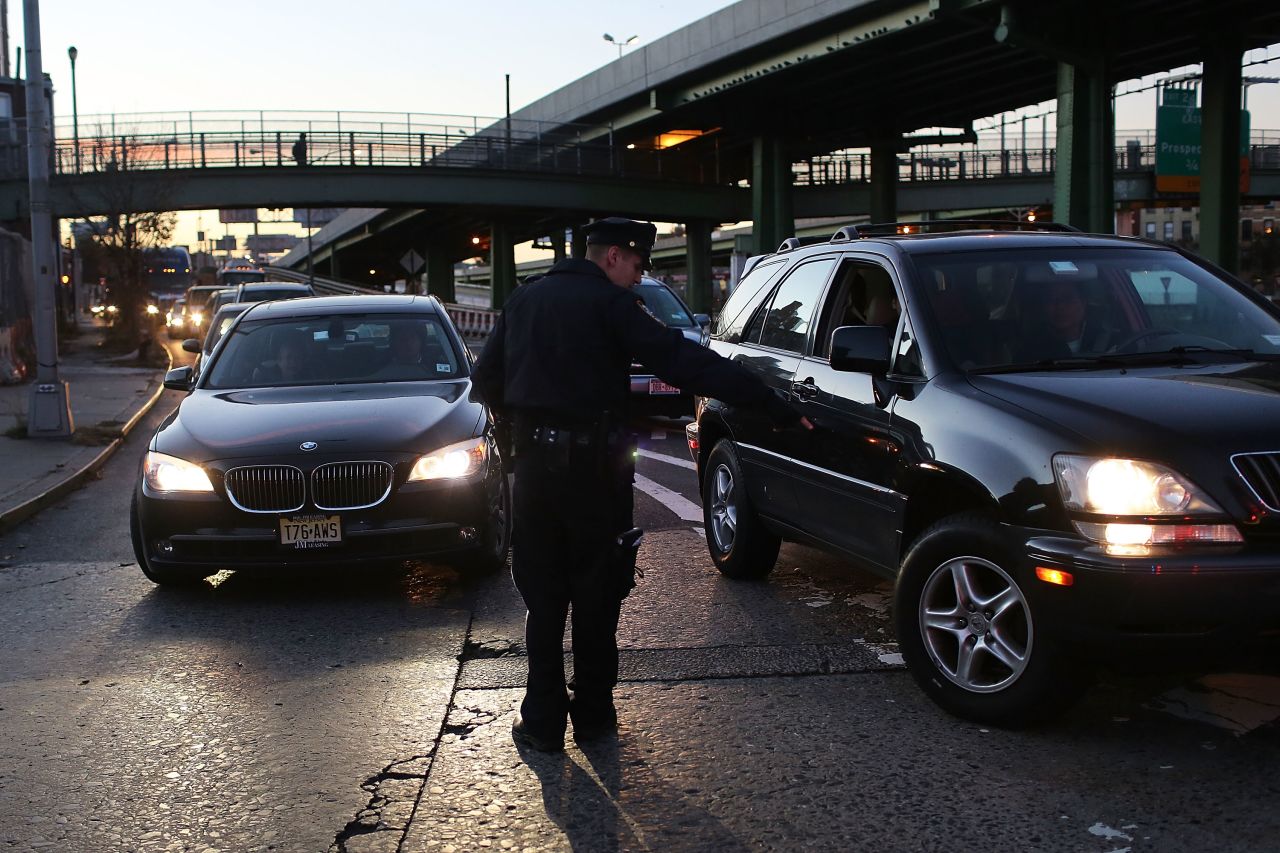 A police officer checks cars entering the Brooklyn Queens Expressway to confirm that they have three occupants before allowing them to cross into Manhattan on Thursday. Limited public transit has returned to New York, and most major bridges have reopened. However, vehicles must have three occupants to pass.