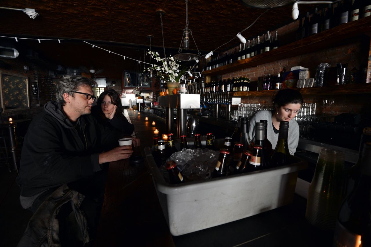 Matthew Mark Meyer, left, and Annie Barwick, center, sit in a darkened Randolf Beer Restaurant which is using generator power to reopen on Friday in New York City.