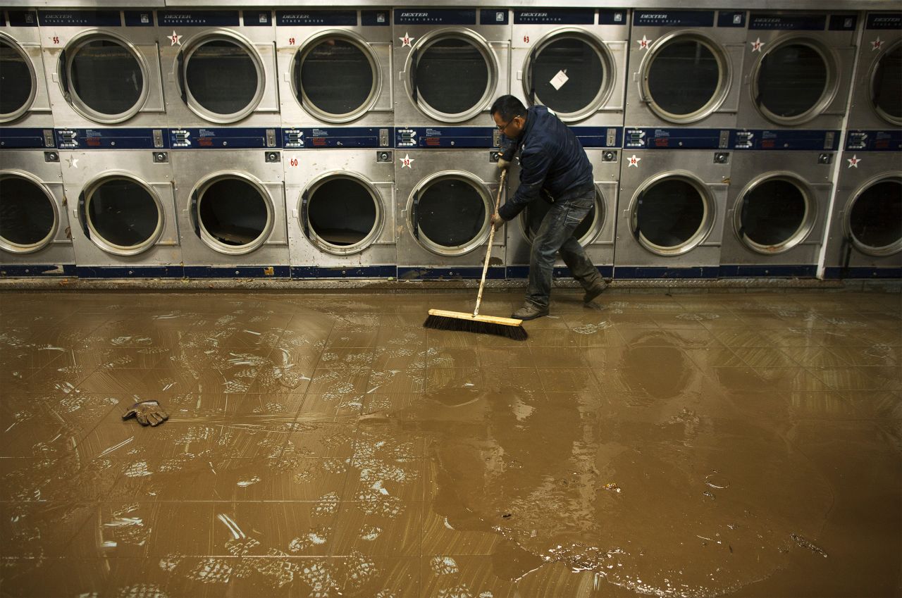 Eddie Liu uses a broom to clean up mud and water from a flooded coin laundry in Coney Island on Friday.
