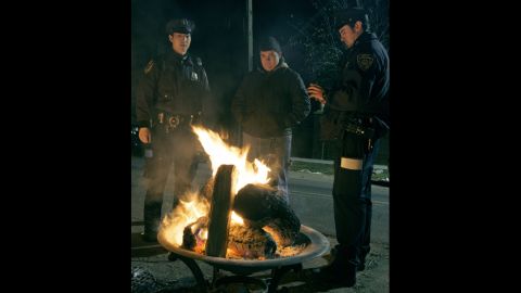 New York City police officers and a resident warm up in front of a fire in a blacked-out area of Oakwood Beach on Staten Island.