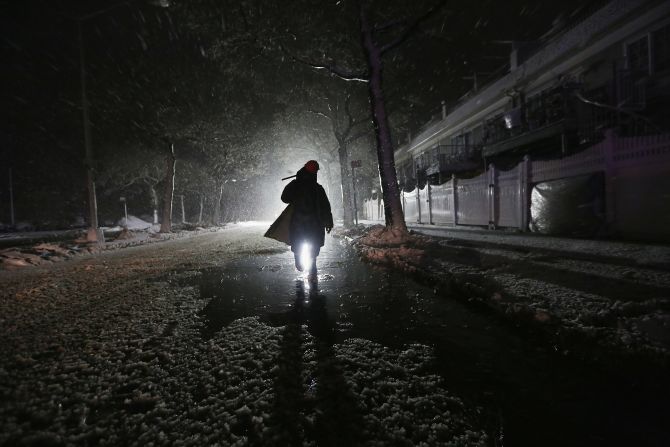 A repair worker is silhouetted by a police spotlight as he walks down a darkened street during a nor'easter on Wednesday in Rockaway.