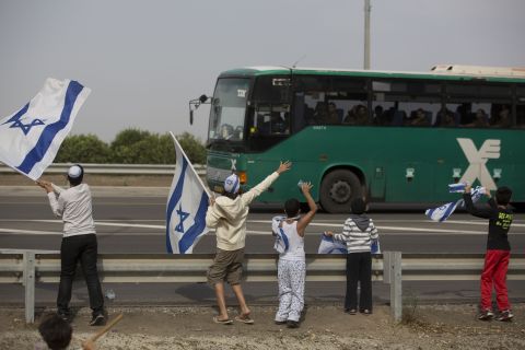 Israeli children wave their national flag Saturday, November 17, as they greet a bus carrying soldiers on a road leading to the Israel-Gaza border near the southern Israeli town of Ofakim.