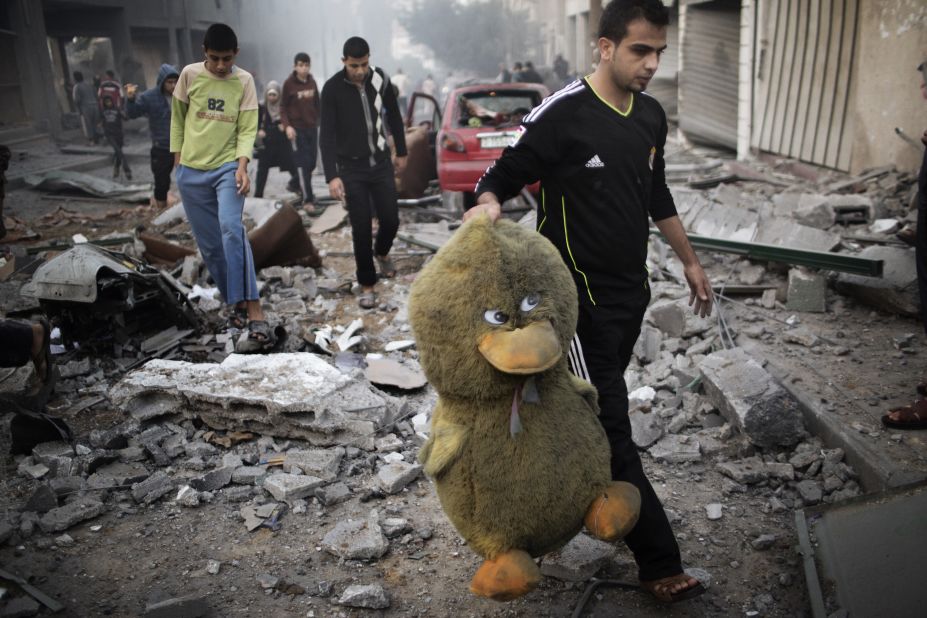A Palestinian man carries a stuffed toy through a street littered with debris after an air raid on a sporting center in Gaza City on Monday.