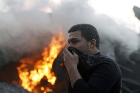 A man covers his nose and mouth as he passes burning debris after Israeli airstrikes in Gaza City on Monday.