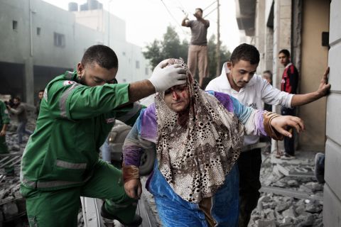 A paramedic helps a Palestinian woman out of her building, which was damaged during an Israeli air raid on a nearby sporting center in Gaza City on Monday. At least 90 Palestinians, including a family of 10, have been killed, officials say.