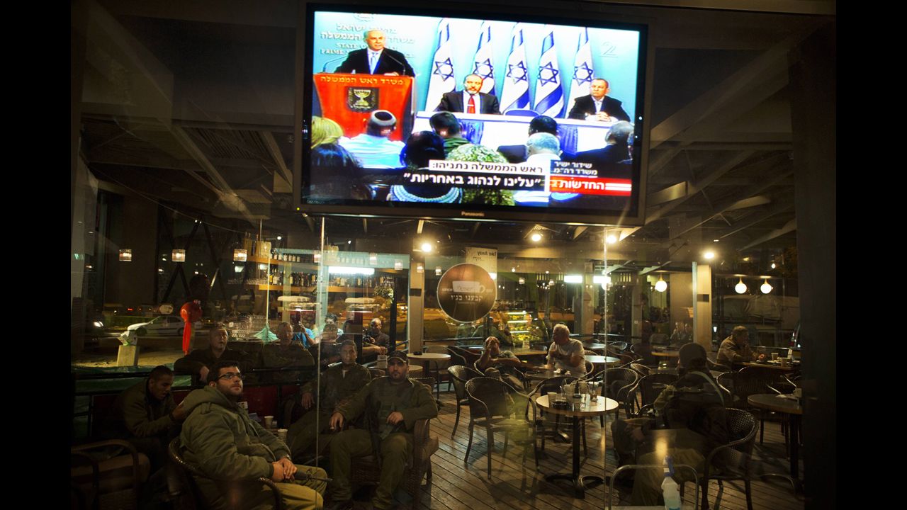 Israeli soldiers sit in a restaurant at the Yad Mordechay Junction as they watch Israeli Prime Minister Benjamin Netanyahu deliver a statement on live television from Jerusalem.