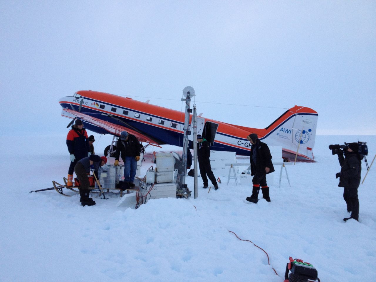 The crew at an ice core drill site after landing safely on the ice. The drilling has to be performed at night because the surface is so slushy from ice melt during daylight that the plane would sink in and get stuck.