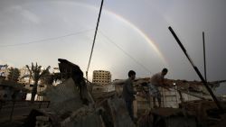 Palestinians inpect the rubble of a destroyed house as a rainbow arcs over Gaza City on November 23, 2012.