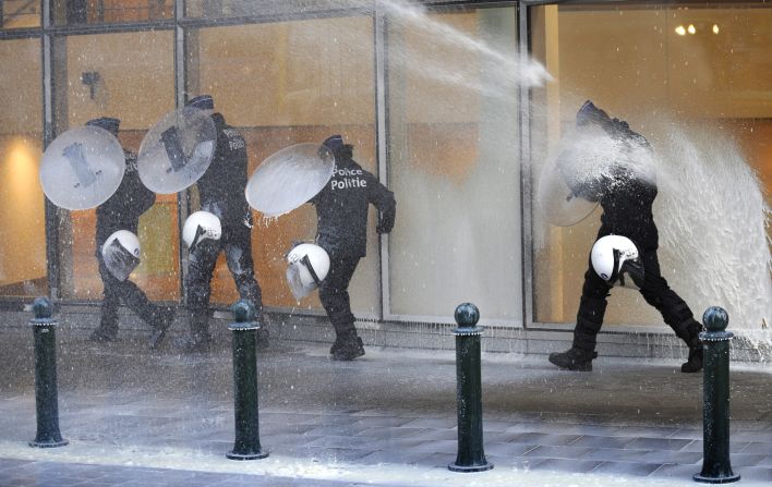Police officers walk in front of the government building Monday, using shields to protect themselves from the milk.