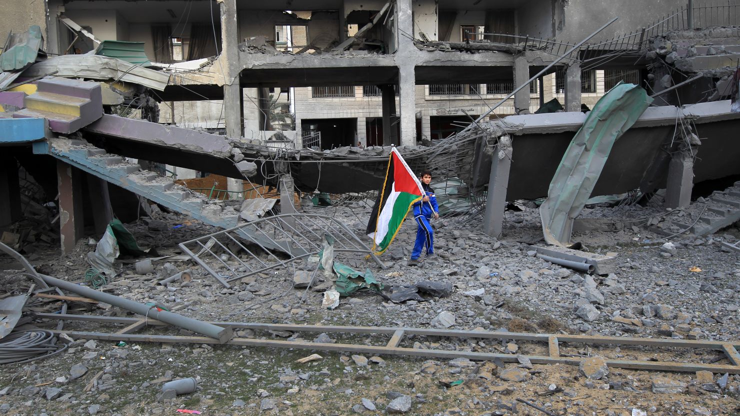 A Palestinian boy carries the national flag as he makes his way through the debris of the destroyed Palestine Stadium.