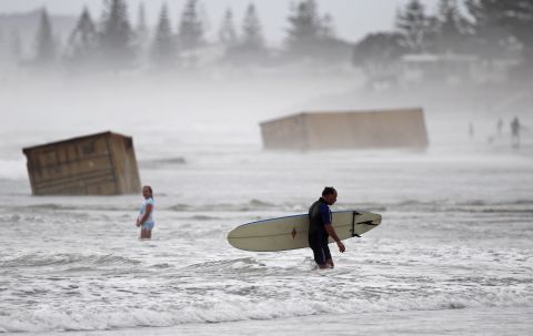 <strong>January 10: </strong>A surfer walks past cargo containers washed ashore from the stricken container ship Rena at Waihi Beach in New Zealand. The ship was stranded on a reef for more than three months before breaking up and sinking in rough seas, littering beaches with cargo and debris.