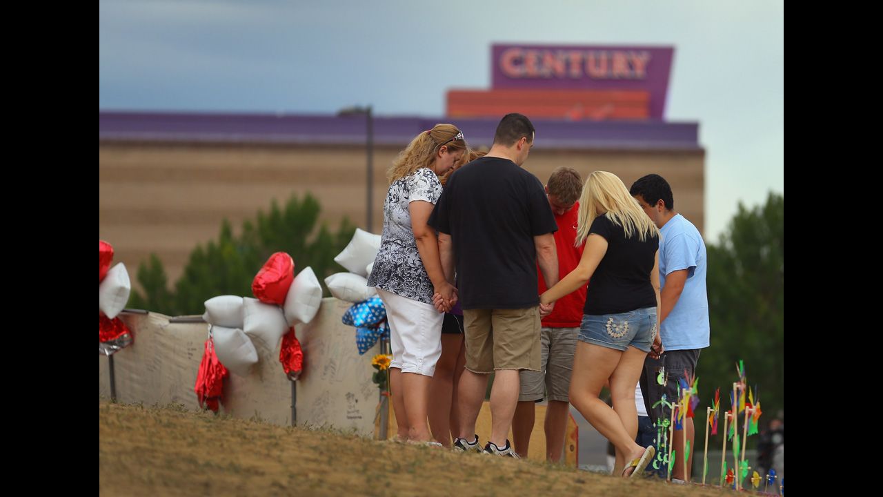<strong>July 28:</strong> Visitors gather and pray around a cross erected at a memorial set up across the street from the Century 16 movie theater in Aurora, Colorado. James Holmes is suspected of killing 12 people and injuring 58 others during a shooting rampage on July 20 at a screening of "The Dark Knight Rises."