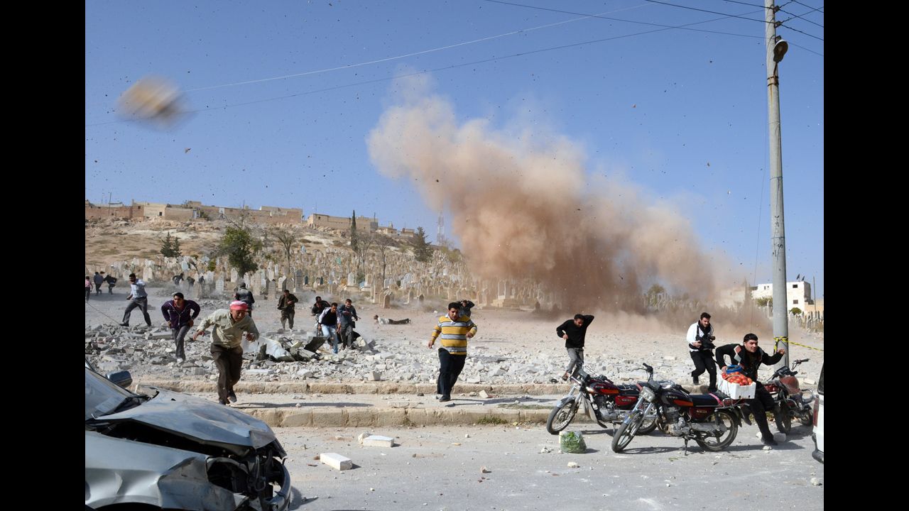 <strong>November 4:</strong> Syrians take cover as a second bomb explodes during a rescue attempt in a nearby building that was hit during an air raid by government forces in the northern city of Al-Bab.