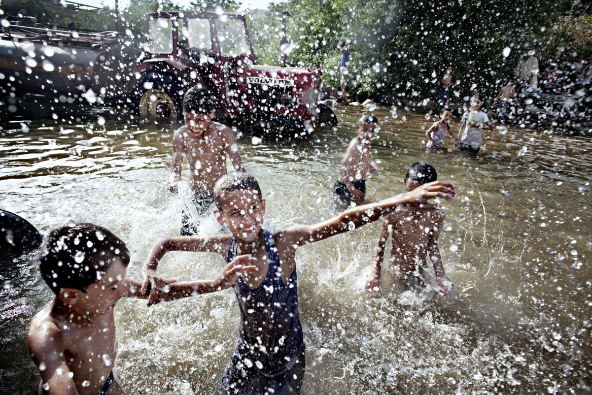 <strong>June 15:</strong> Lebanese children and Syrian refugees play in a natural spring close to the Syrian border. Behind them, a line of trucks and tractors collect fresh water to supply villages in the area. Tens of thousands of people have fled from Syria to Lebanon since the conflict started.