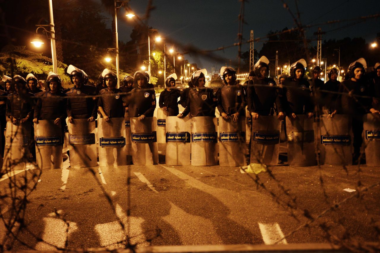Egyptian riot police stand behind barbwire as thousands of Egyptian demonstrators march to the presidential palace in Cairo, Egypt, on Tuesday, December 4.