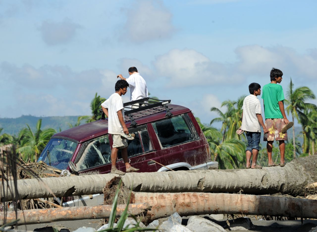 Residents stand next to a vehicle washed up among debris along a river in New Bataan on December 6.