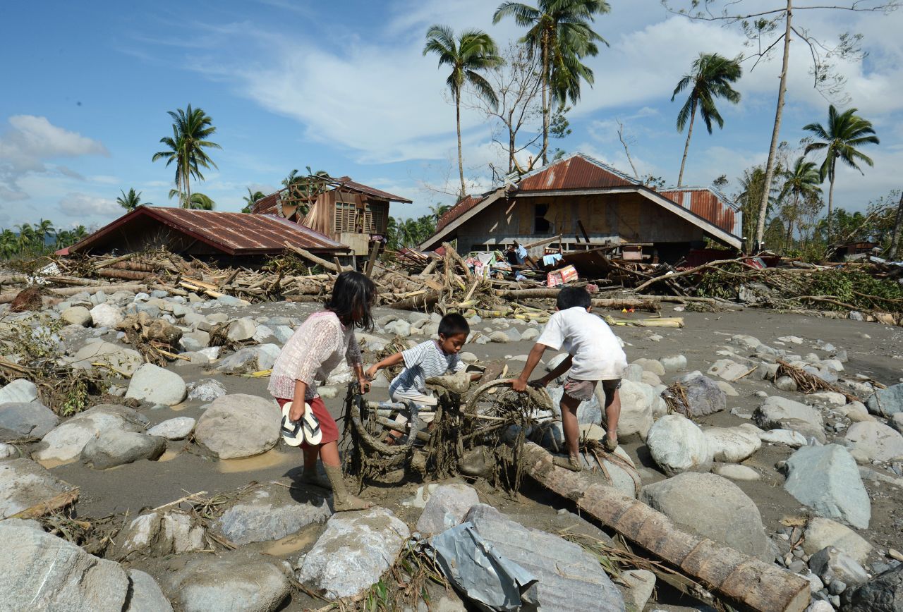 Children retrieve a bicycle among boulders near destroyed houses in New Bataan on December 6.