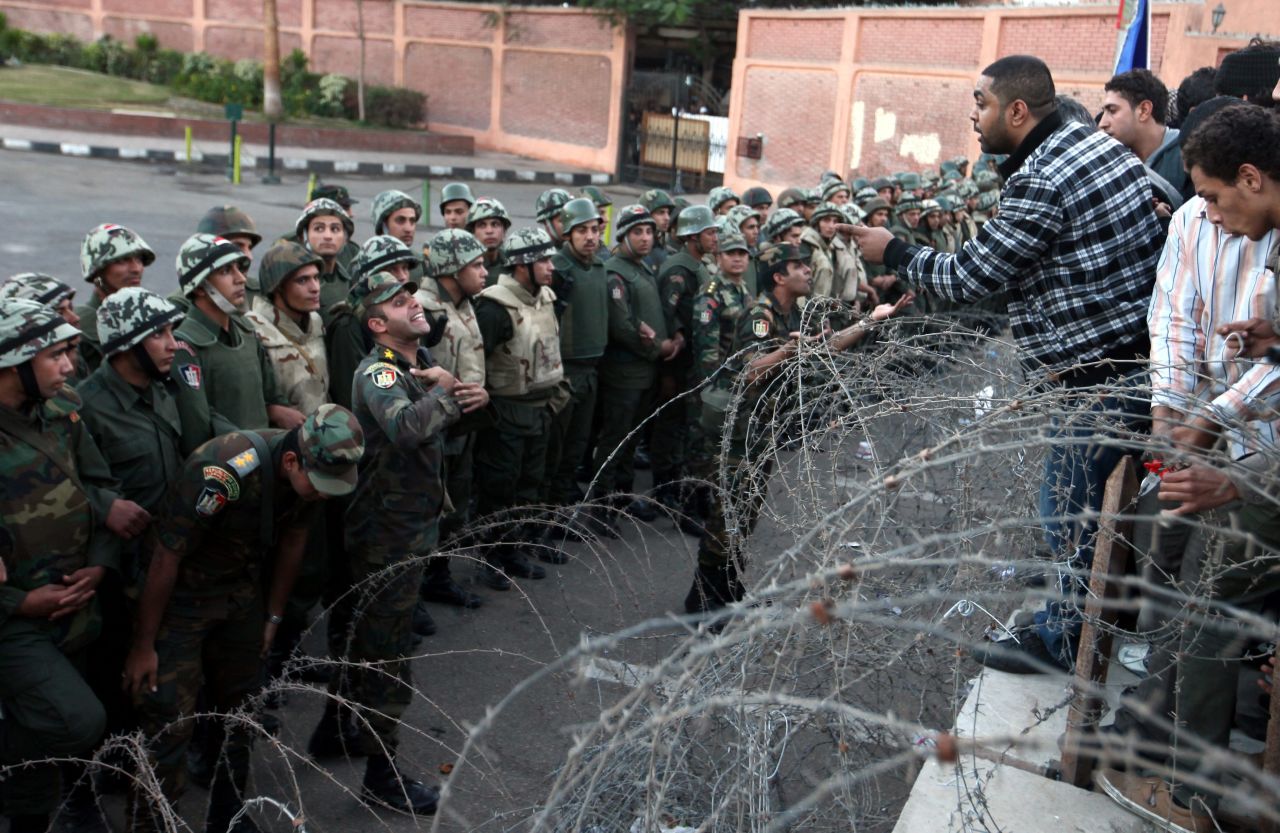 A protester tries to climb over a barbed-wire fence as Egyptian soldiers stand guard during a demonstration near the presidential palace in Cairo on Friday, December 7.