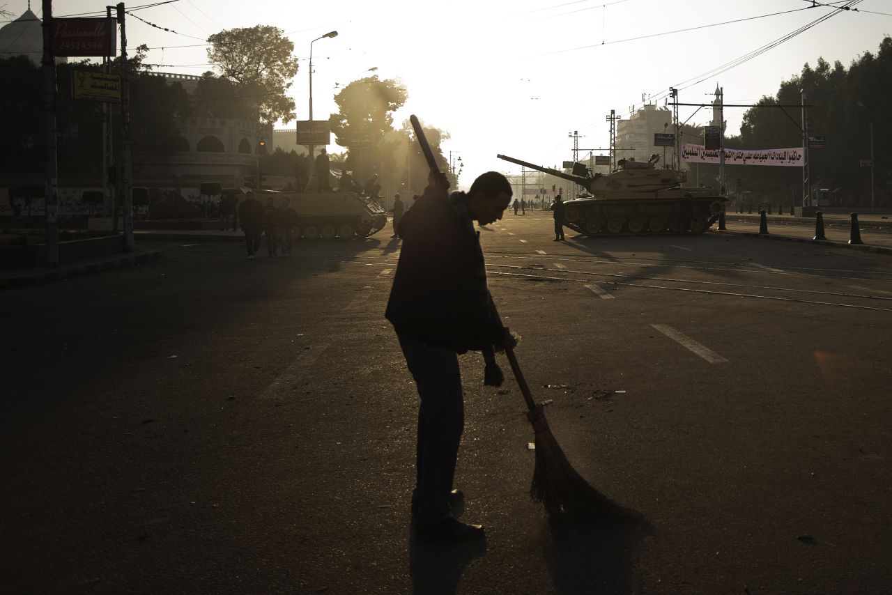 An Egyptian protester sweeps the street near army tanks deployed outside the presidential palace in Cairo on December 8, after continued protests overnight.