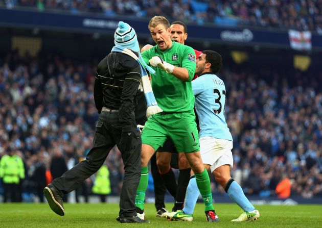 Manchester City goalkeeper Joe Hart of  confronts a pitch invader at the end of his side's 3-2 derby defeat by Manchester United, whose defender Rio Ferdinand (at back) was left with a bloody face after being hit by a coin thrown from the crowd. 