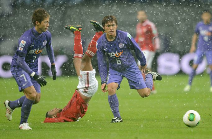 Al-Ahly midfielder Hossam Ashour takes a tumble as he fights for the ball with Sanfrecce Hiroshima's Toshihiro Aoyama (right) and Koji Morisaki (left) in the snowy conditions.