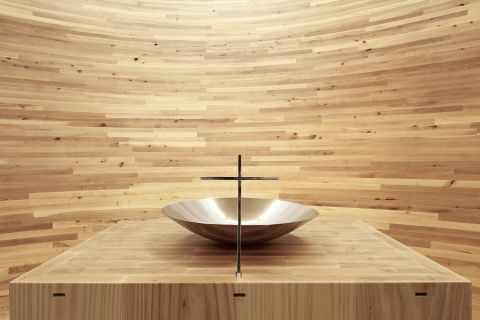 Inside the Kamppi Chapel, the curving inner wall is made out of alder planks into a closed space with light falling from above.