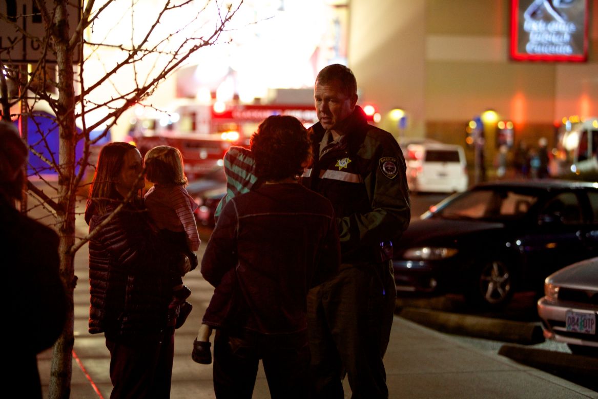 A law enforcement officer talks to people waiting outside the mall.