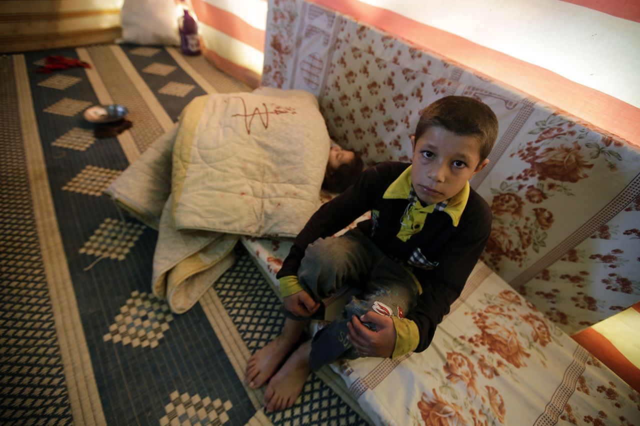 A Syrian refugee child sits near his sleeping sister at his family's makeshift house built on an agricultural field in Saadnayel in the Lebanese Bekaa valley on December 12, 2012.