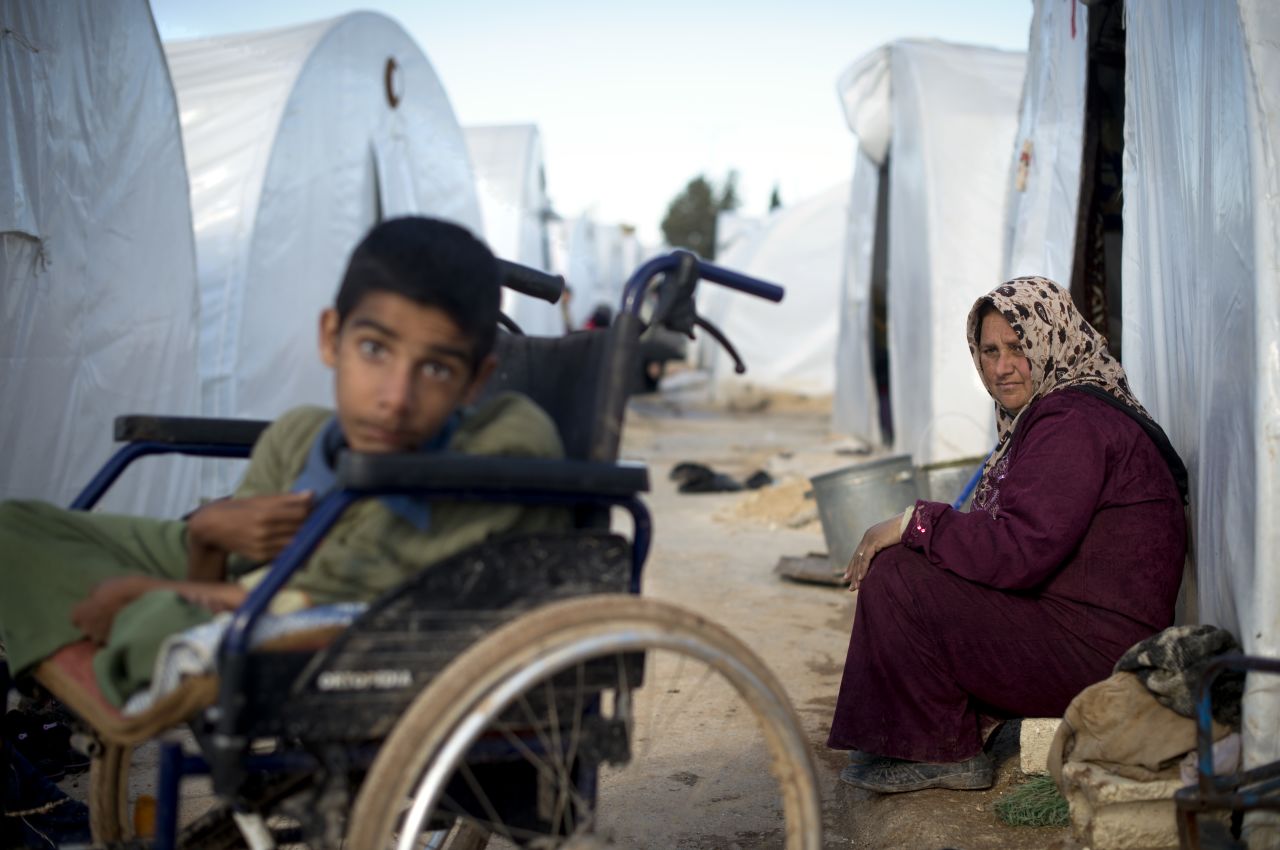 A mother looks over at her disabled child sitting among plastic tents in a refugee camp on the border between Syria and Turkey near the northern city of Azaz on December 5, 2012.