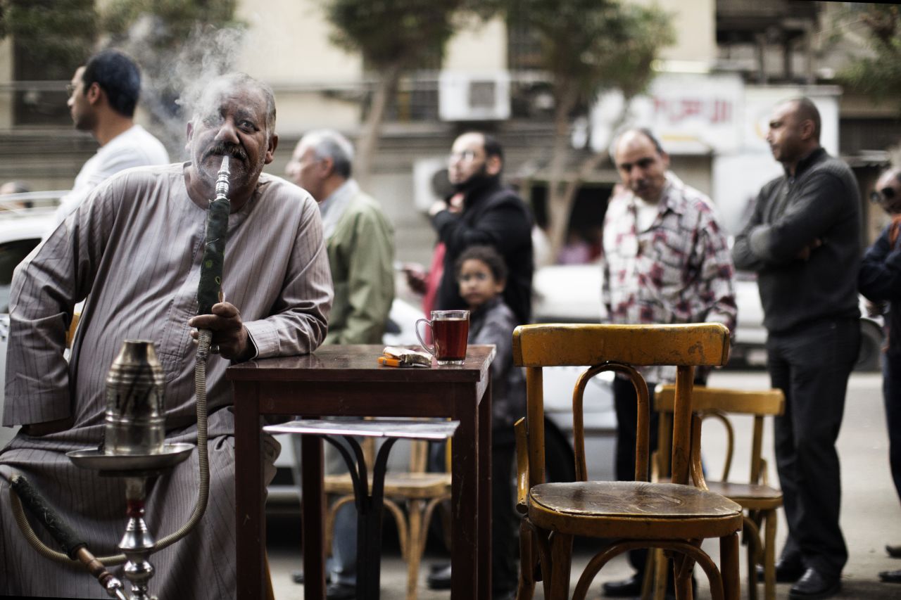 An Egyptian man smokes a waterpipe, known locally as Shisha, as others queue outside a polling station in central Cairo to cast their votes on a new constitution.