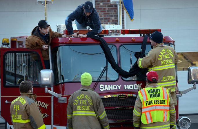Firefighters attach black bunting to a fire truck as a memorial at the fire station down the street from the Sandy Hook Elementary School in Newtown, Connecticut, on Saturday, December 15.