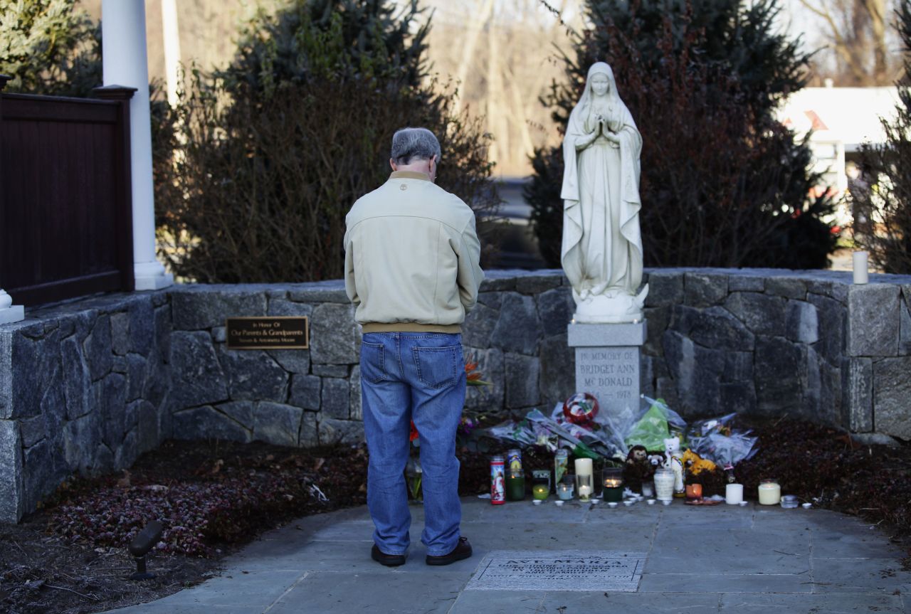 A man bows his head as he stands at a makeshift memorial, outside Saint Rose of Lima Roman Catholic Church in Newtown on Saturday, December 15.
