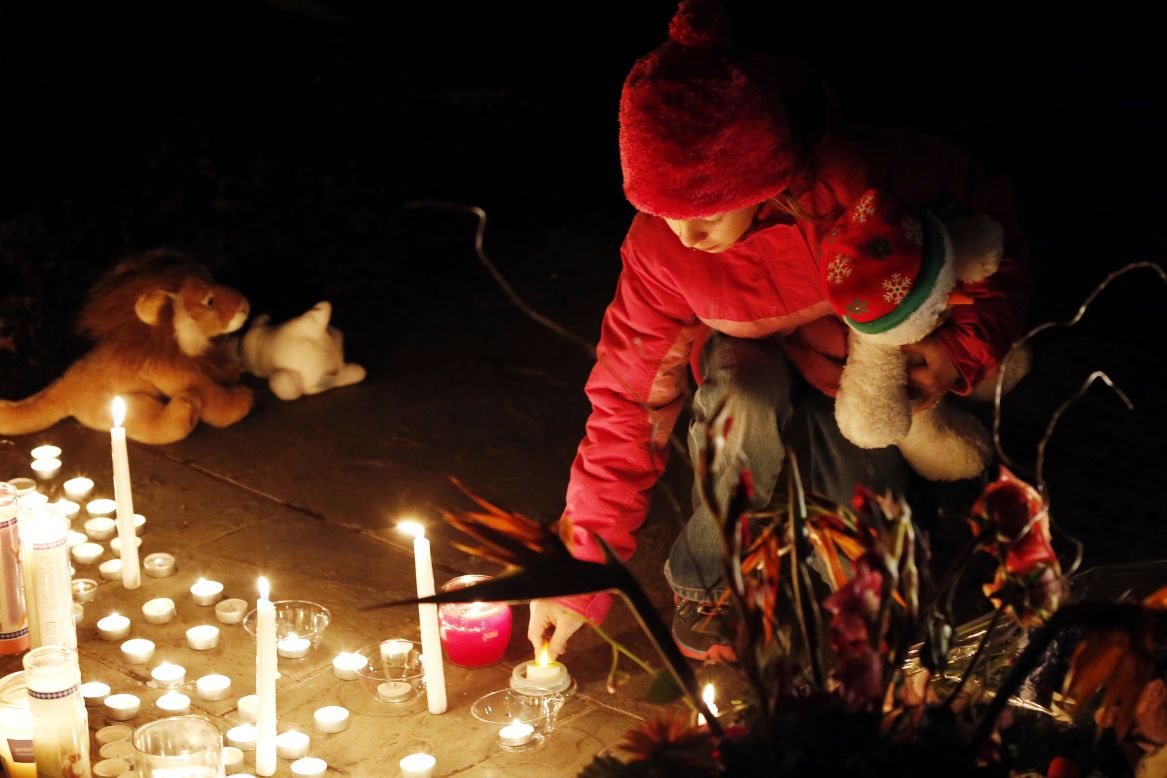 A child lights a candle at a memorial filled with flowers, stuffed toys and candles outside of Saint Rose of Lima Church near Sandy Hook Elementary School in Newtown, Connecticut on Saturday.