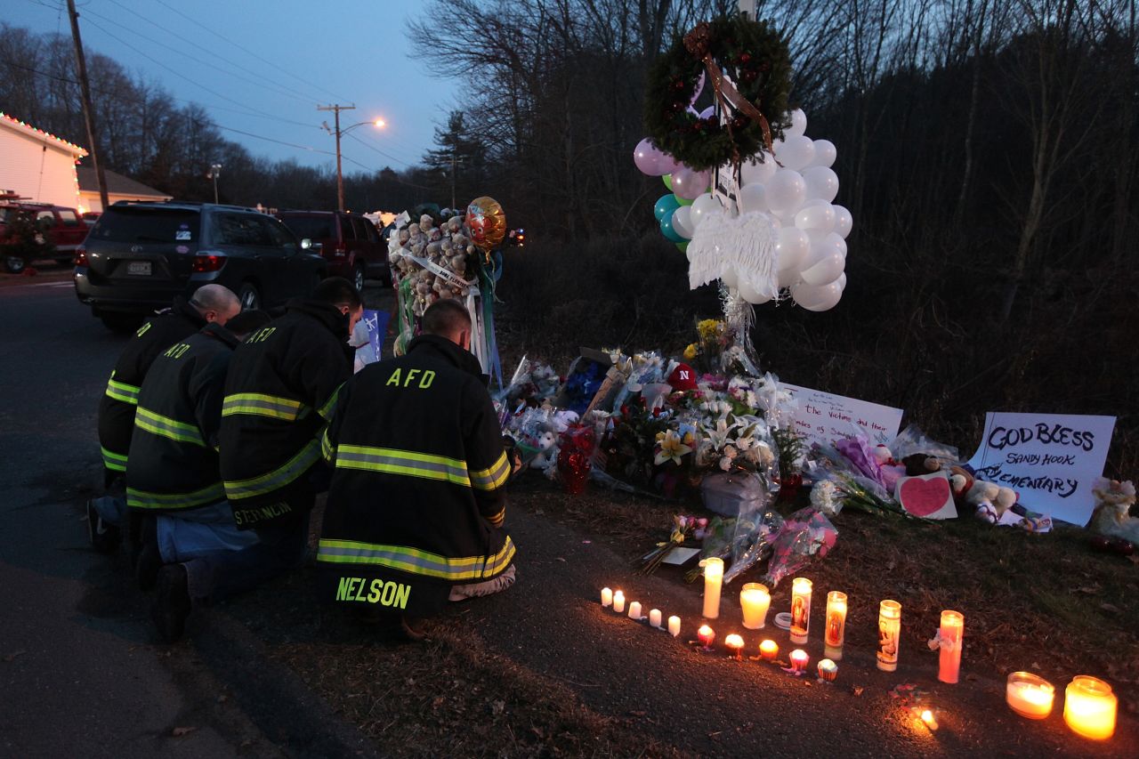 Firefighters kneel to pay their respects at a makeshift memorial near the school in Newtown on Saturday.