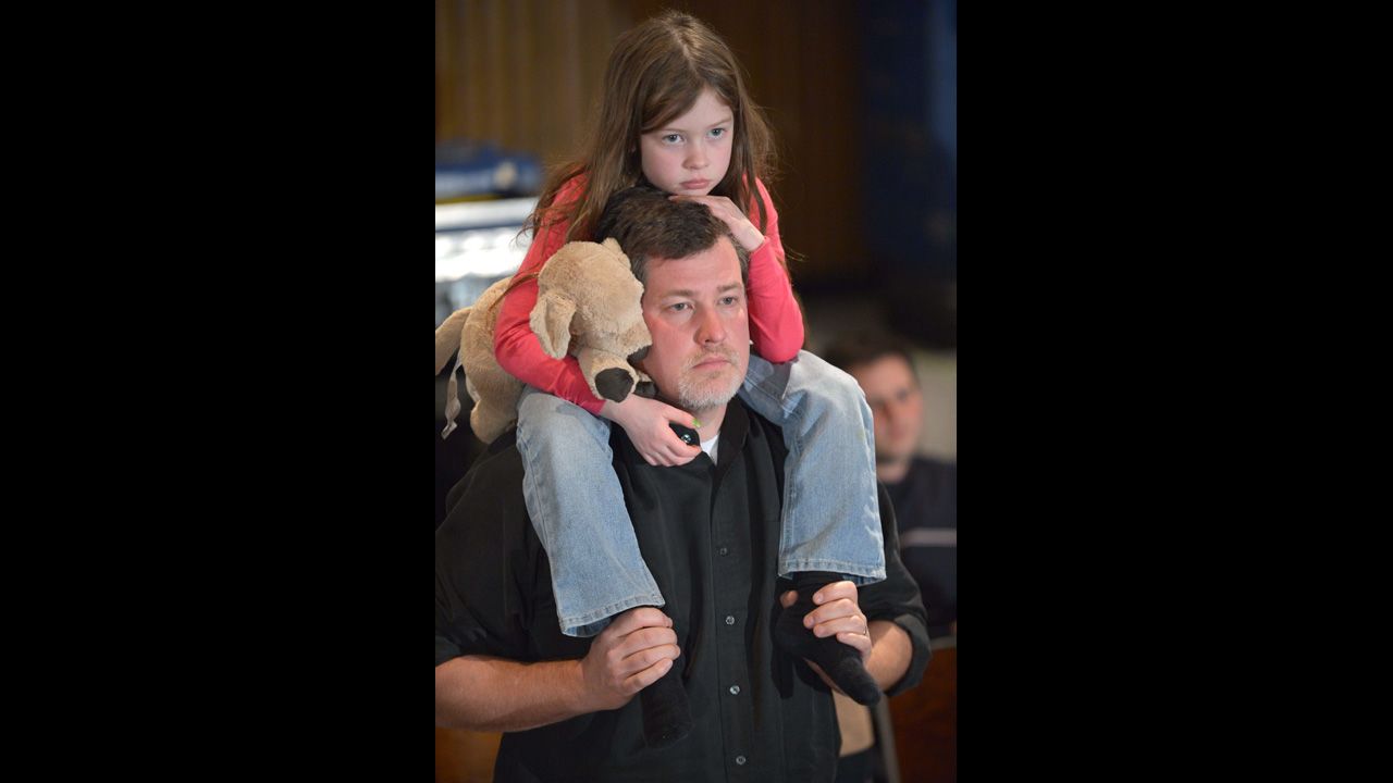A little girl clutches a plush toy dog as she rides on her father's shoulders into the Newtown High School auditorium.