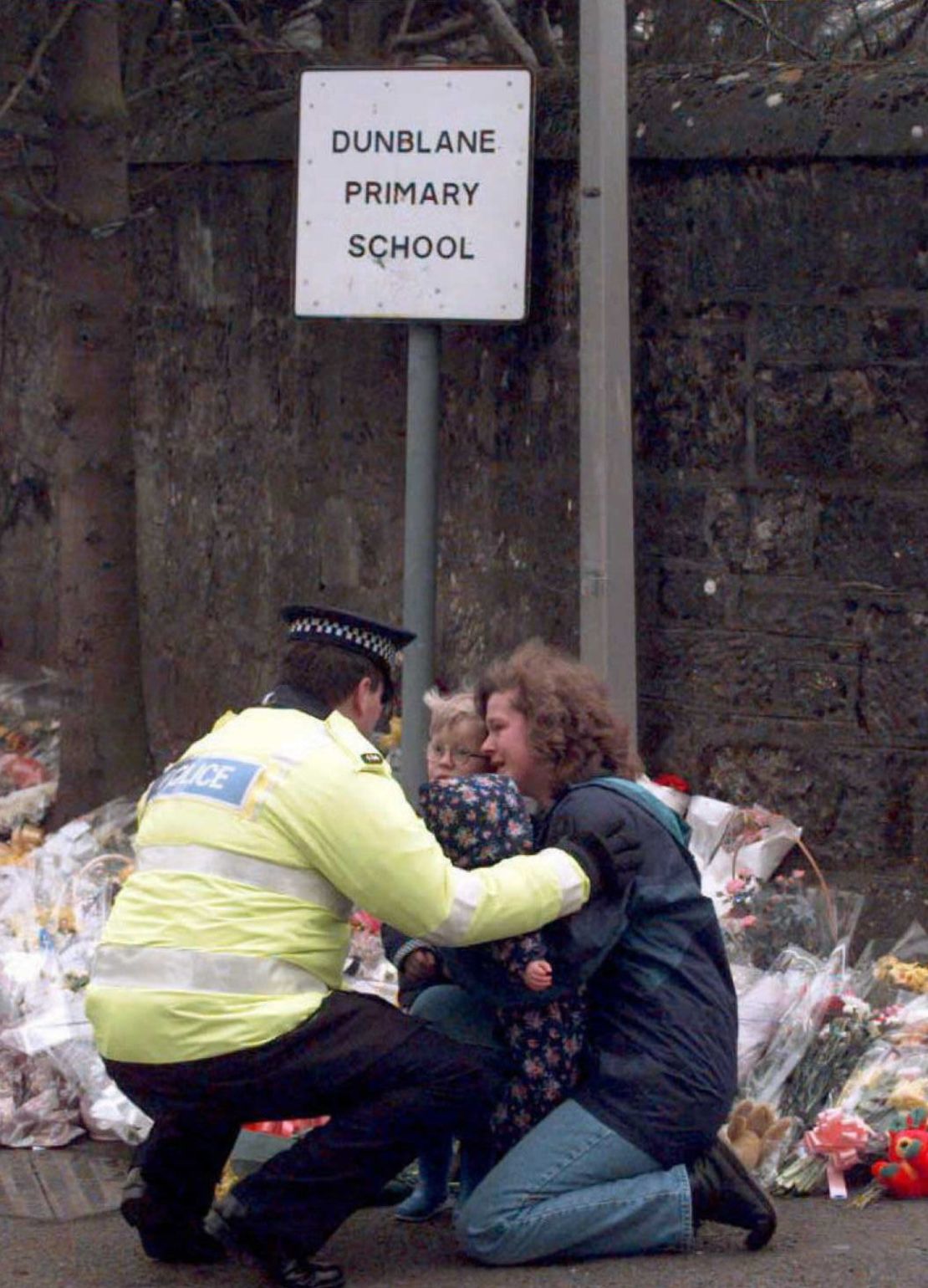 A policeman consoles a mother and her children after they had laid a bouquet outside the school where 16 children and their teacher were killed in Dunblane.
