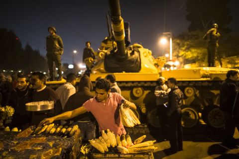 A street vendor grills corn as Egyptian soldiers stand guard at the Presidential Palace on Tuesday, December 18, in Cairo. Protesters opposed to President Mohamed Morsy's first round of voting in the constitutional referendum gather during continuing demonstrations. 