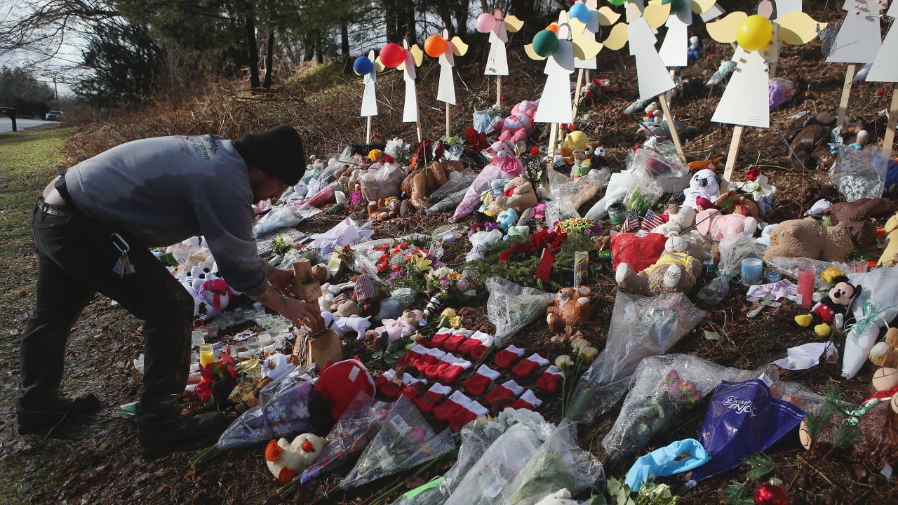 NEWTOWN, CT - DECEMBER 21:  A mourner places a carved wooden cross at a streetside memorial on December 21, 2012 in Newtown, Connecticut. Church bells rang out at 9:30 EST to mark the one-week anniversary of the Sandy Hook Elementary School massacre.  (Photo by John Moore/Getty Images)