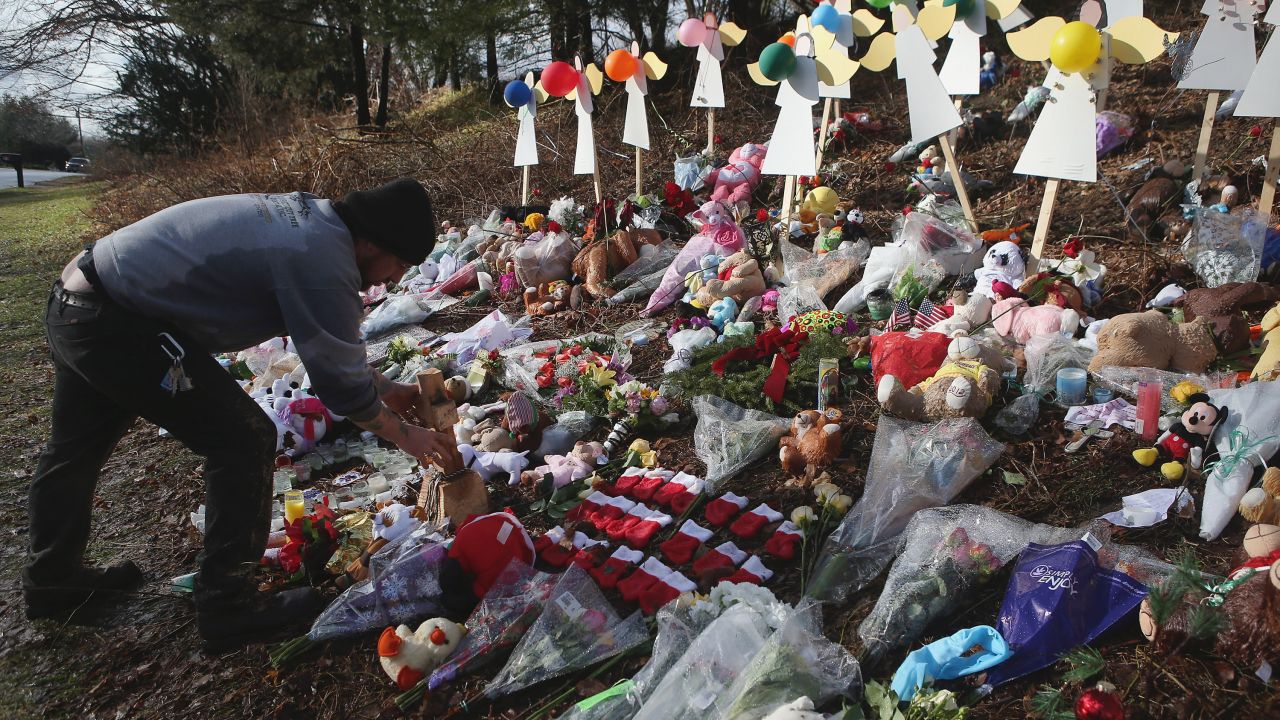 NEWTOWN, CT - DECEMBER 21: A mourner places a carved wooden cross at a streetside memorial on December 21, 2012 in Newtown, Connecticut. Church bells rang out at 9:30 EST to mark the one-week anniversary of the Sandy Hook Elementary School massacre. (Photo by John Moore/Getty Images)