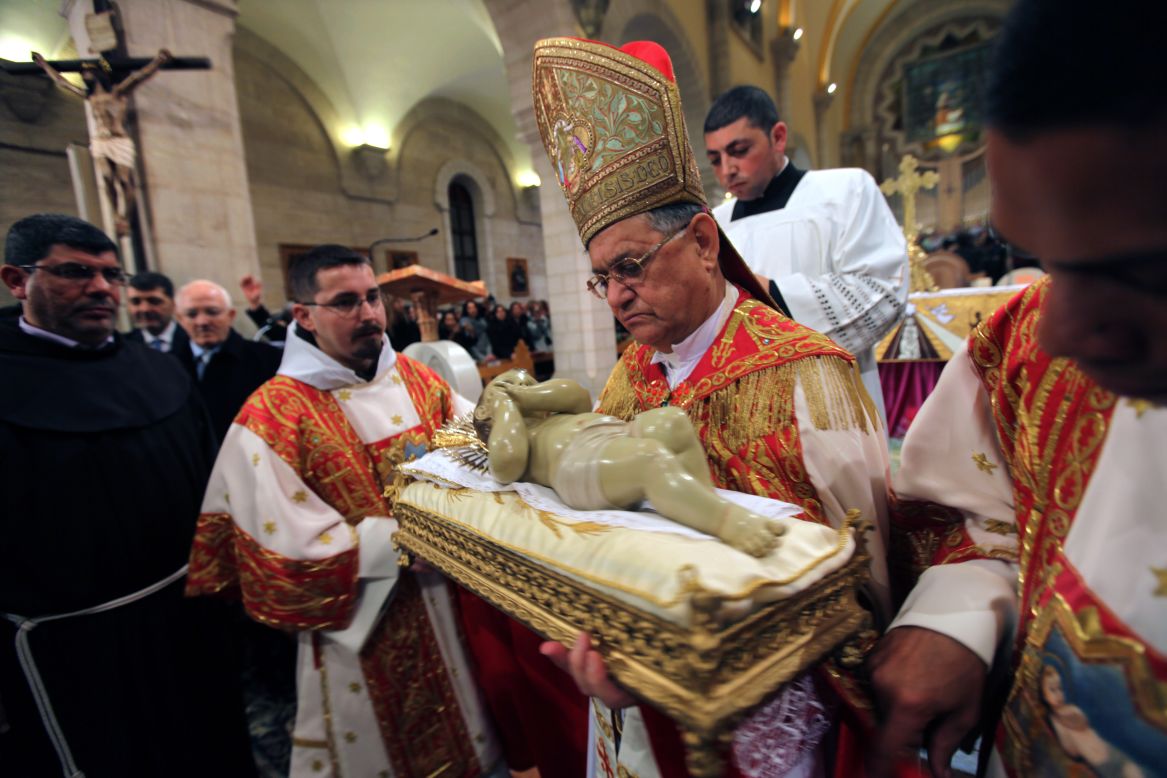 Fouad Twal, the Latin patriarch of Jerusalem, holds a  statue of the baby Jesus at the end of the Christmas midnight Mass at the Church of St. Catherine in Bethlehem, West Bank. He walks in a procession to the Grotto of the Nativity, in the adjacent Church of the Nativity, where Christians believe the Virgin Mary gave birth to Jesus Christ.