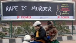 Female commuters ride a scooter past a billboard, calling for capital punishment against rape, in New Delhi on December 27, 2012.