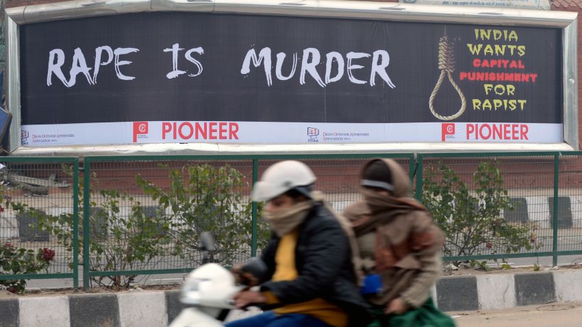Female commuters ride a scooter past a billboard, calling for capital punishment against rape, in New Delhi on December 27, 2012.